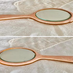 May include: Two vintage oval hand mirrors with pink plastic handles and silver-toned glass mirrors.