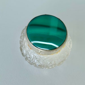 May include: A clear, cut-glass perfume bottle with a silver rim and a circular green and white stone top. The bottle has a diamond-cut pattern. The stone top is a vibrant green with white stripes.