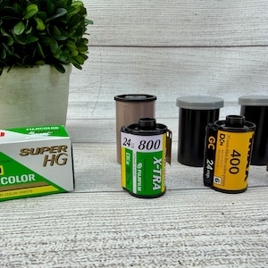 May include: A green and white box of Fujicolor Super HG 1600 film, a green Fujifilm X-TRA 800 film canister, and two yellow Fujifilm 400 film canisters with black plastic caps, all designed for 35mm color photography and 24 exposures.