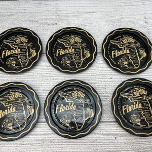 May include: Six black and gold coasters with a map of Florida and the text "Orange Blossom, Gulf of Mexico, Florida" on each coaster.