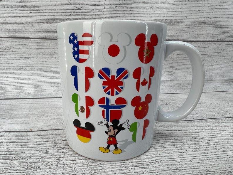 Puede incluir: Taza de cer&aacute;mica blanca con asa. La taza presenta un dise&ntilde;o de Mickey Mouse con banderas de diferentes pa&iacute;ses del mundo. Las banderas incluyen Estados Unidos, Jap&oacute;n, Reino Unido, Canad&aacute;, M&eacute;xico y China.