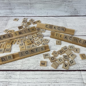 May include: A close-up of a wooden surface with a collection of wooden letter tiles spelling out the names "MRS. SMITH", "JONES", "COACH", and "TEACHER".