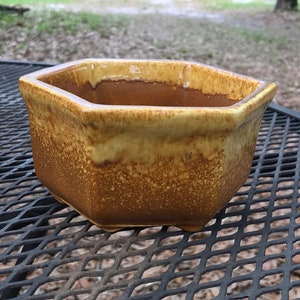 May include: A hexagonal ceramic planter with a brown and yellow glaze. The planter is sitting on a black metal table.