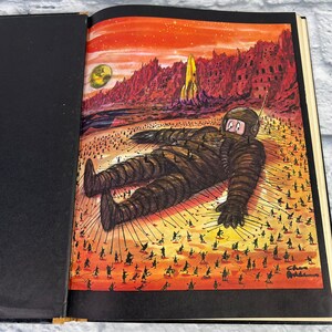 May include: A vintage illustration of a giant astronaut lying on a red and orange desert landscape. Tiny figures are pulling on ropes attached to the astronaut's body. The illustration is signed "Chas Addams".