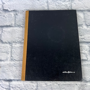 May include: A black hardcover book with a gold spine. The book has a white signature on the front cover that reads "Alan Alda".