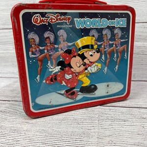 May include: Red metal lunchbox featuring Mickey and Minnie Mouse ice skating. The lunchbox has a handle and says "Walt Disney Productions' World on Ice" on the front.