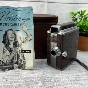 May include: A vintage brown and silver 8mm movie camera with a leather case and a pamphlet that reads "Briskin 8 Magazine Movie Camera It's New!"