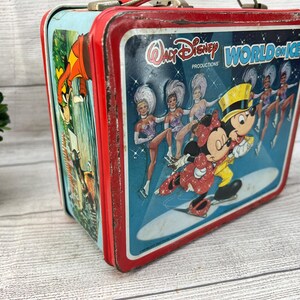 Op de afbeelding: Vintage metalen lunchbox met een rood frame en een blauwe achtergrond. De lunchbox toont Mickey en Minnie Mouse schaatsen, met de tekst "Walt Disney World on Ice". Het zijpaneel heeft een cartoon illustratie.
