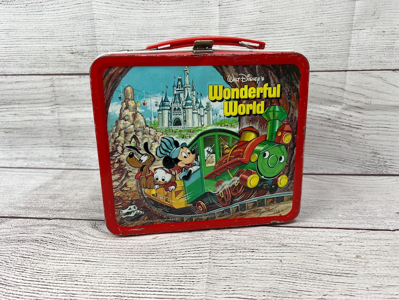 May include: Red metal lunchbox featuring a vintage illustration of Mickey Mouse and friends riding a train through a whimsical landscape. The lunchbox has the words "Walt Disney's Wonderful World" printed on the front.