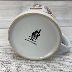 Puede incluir: Taza de cer&aacute;mica blanca con un dise&ntilde;o colorido con Mickey Mouse y otros personajes de Disney. La parte inferior de la taza tiene una imagen en blanco y negro del castillo de Disney y el texto "Walt Disney World&reg; &copy; Disney Hecho en Tailandia".