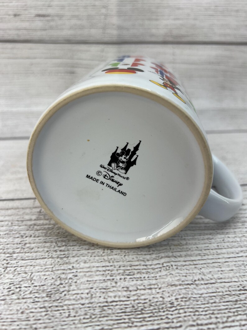Puede incluir: Taza de cer&aacute;mica blanca con un dise&ntilde;o colorido con Mickey Mouse y otros personajes de Disney. La parte inferior de la taza tiene una imagen en blanco y negro del castillo de Disney y el texto "Walt Disney World&reg; &copy; Disney Hecho en Tailandia".
