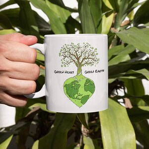 May include: White ceramic mug with a green tree growing out of a green heart-shaped earth. The text "Green Heart" and "Green Earth" are written on the mug.
