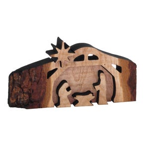 May include: A wooden nativity scene cutout with a brown and black finish. The scene depicts the baby Jesus in a manger with Mary and Joseph standing nearby. A star is above the manger.