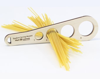May include: A wooden spaghetti serving measure with a handle and three circular holes for measuring portions. The measure has the text "Spaghetti Serving Measure Maple Landmark" printed on it. Spaghetti noodles are inserted into the holes for demonstration.