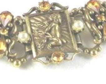 Könnte beinhalten: Ein goldfarbenes Metallgliederarmband mit rechteckigen Elementen, die geprägte Puttenfiguren zeigen, verziert mit bernsteinfarbenen tropfenförmigen und runden Kristallen sowie kleinen weißen Kunstperlen zwischen den dekorativen Gliedern.