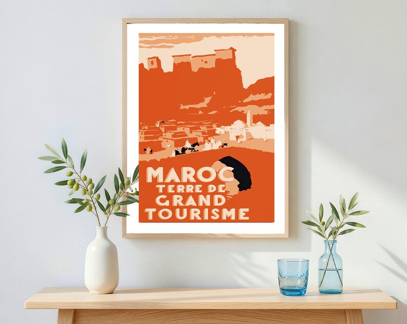 May include: A framed travel poster featuring a stylized orange and cream illustration of a Moroccan landscape with buildings and figures. The text MAROC TERRE DE GRAND TOURISME is printed in bold, light-colored capital letters at the bottom.