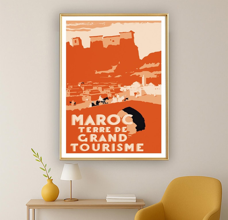 May include: A rectangular wall art print featuring a stylized orange and cream illustration of a Moroccan landscape with buildings and figures. The text MAROC TERRE DE GRAND TOURISME is printed in bold cream letters at the bottom of the poster.