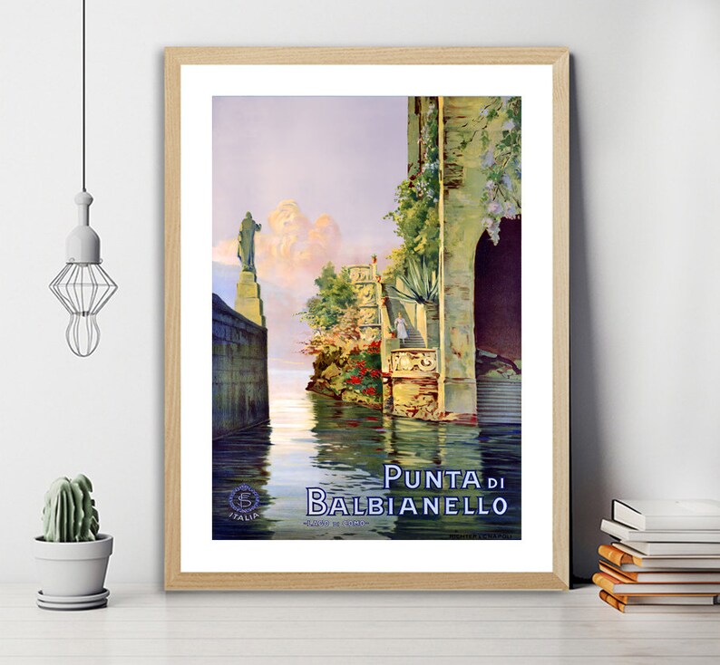 May include: Vintage travel poster featuring a scenic view of Punta di Balbianello, a picturesque location in Italy. The poster depicts a stone building with a lush garden and a calm body of water in the foreground. The text "Punta di Balbianello" is prominently displayed at the bottom of the poster.