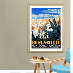 May include: A framed vintage travel poster for Beausoleil, Monte-Carlo Sup&eacute;rieur. The poster features a vibrant illustration of a coastal town with red-tiled roofs, a blue sky, and large green plants. The poster has a wooden frame.