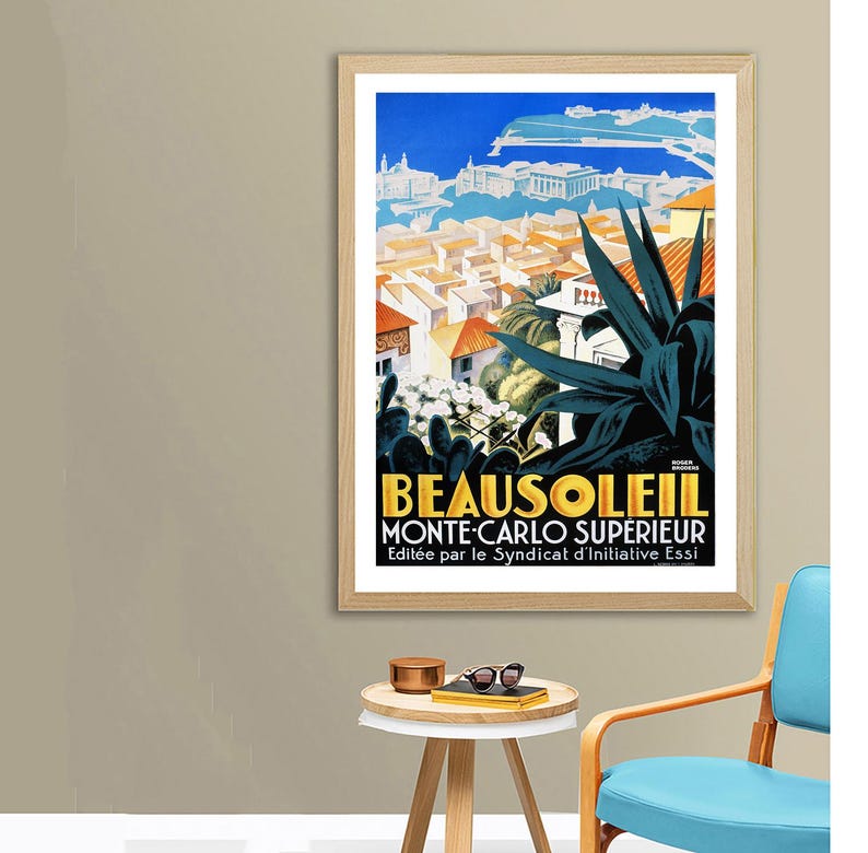 May include: A framed vintage travel poster for Beausoleil, Monte-Carlo Sup&eacute;rieur. The poster features a vibrant illustration of a coastal town with red-tiled roofs, a blue sky, and large green plants. The poster has a wooden frame.