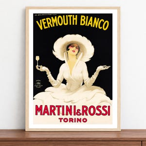 Può includere: Un poster in stile vintage raffigurante una persona con un abito bianco e un cappello a tesa larga che tiene in mano un bicchiere. Il testo recita VERMOUTH BIANCO in alto e MARTINI & ROSSI TORINO in basso, su sfondo nero in cornice.