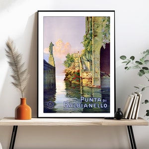 May include: Vintage travel poster featuring a scenic view of Punta di Balbianello, a beautiful Italian destination. The poster depicts a narrow waterway with a stone building on the right and a statue on the left. The water is calm and reflective, and the sky is a soft blue with fluffy clouds. The text "Punta di Balbianello" is prominently displayed in blue lettering.