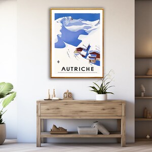 May include: A vintage travel poster featuring a snowy mountain scene with a blue sky and the word "AUTRICHE" in black text. The poster is framed in gold and displayed on a wall.