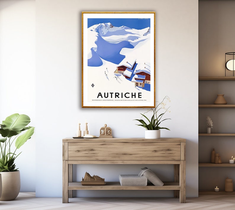 May include: A vintage travel poster featuring a snowy mountain scene with a blue sky and the word "AUTRICHE" in black text. The poster is framed in gold and displayed on a wall.
