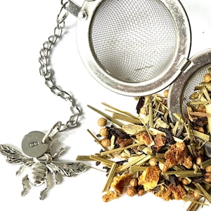 May include: A silver tea infuser with a bee-shaped charm and the letter "B" on it. The infuser is filled with loose leaf tea, including dried orange peel, ginger, and other herbs.