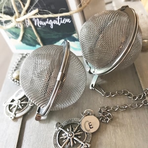 May include: Two silver tea infusers with a chain and compass charms. The infusers are spherical and made of fine mesh. The charms are silver and have a compass design.