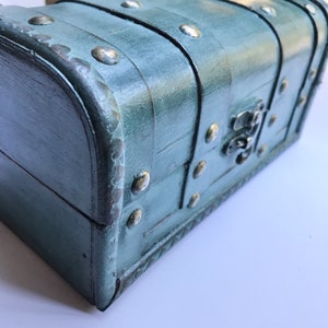 May include: A teal blue wooden treasure chest with metal accents and a decorative metal latch. The chest has a distressed finish and is decorated with a pattern of small metal studs.