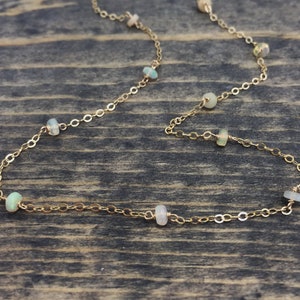 May include: A gold chain necklace with small, white opal beads. The necklace is on a wooden surface.