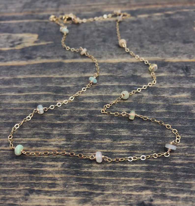 May include: A gold chain necklace with small, white opal beads. The necklace is on a wooden surface.