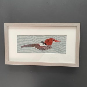 May include: A framed embroidery of a red-headed duck with a small duckling riding on its back. The duck is swimming on a blue and white wavy background.