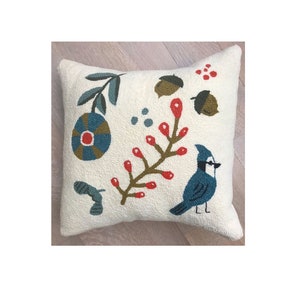 May include: Cream-coloured decorative cushion with an embroidered nature-themed design. Features a blue bird, red berries, green leaves, and acorns. The cushion has a textured surface and a square shape, ideal for adding a touch of nature to any room.