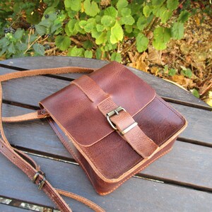 May include: A brown leather crossbody bag with a flap closure and a metal buckle. The bag has a long adjustable strap.