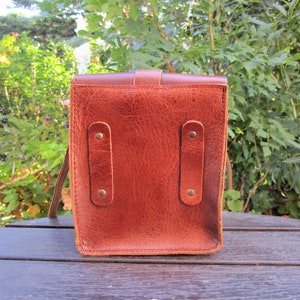 May include: A brown leather bag with two straps on the back. The bag has two metal buckles on each strap.