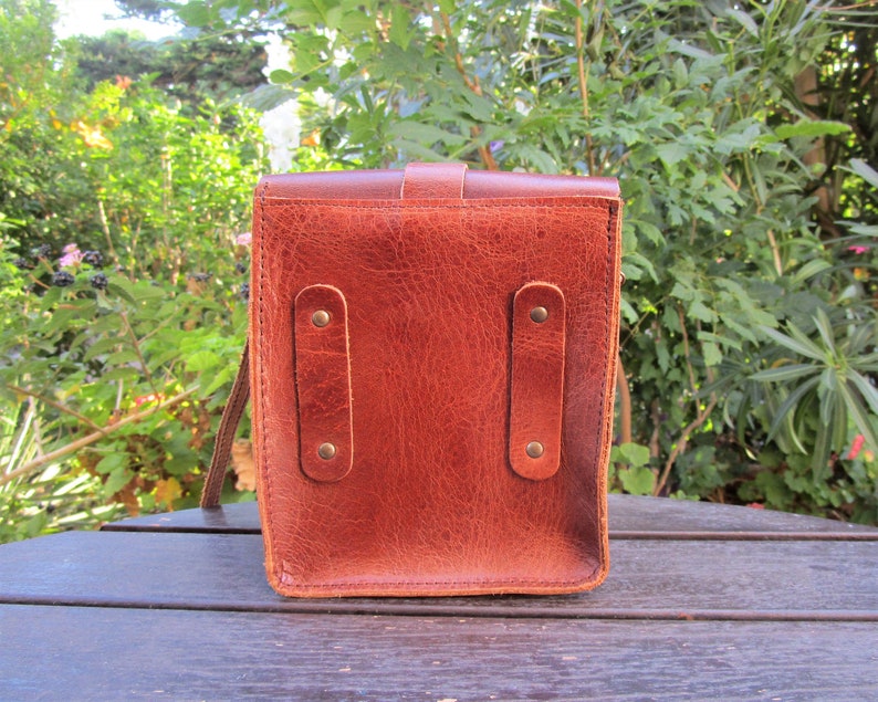 May include: A brown leather bag with two straps on the back. The bag has two metal buckles on each strap.