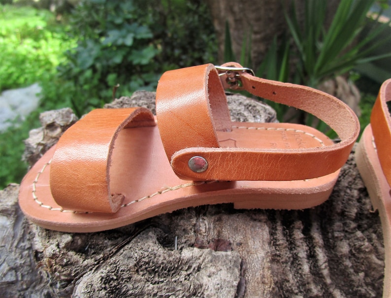 K&ouml;nnte beinhalten: Braune Ledersandalen mit Schnallenverschluss und gen&auml;hter Sohle. Die Sandalen befinden sich auf einer Holzoberfl&auml;che.