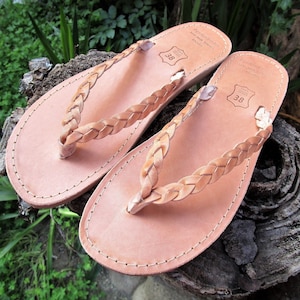 Pu&ograve; includere: Un paio di sandali in pelle color cuoio con cinturini intrecciati. I sandali hanno un design semplice e sono realizzati in pelle di alta qualit&agrave;.