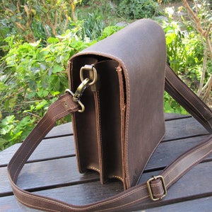 May include: A brown leather messenger bag with a long adjustable strap. The bag has a flap closure and a metal clasp.