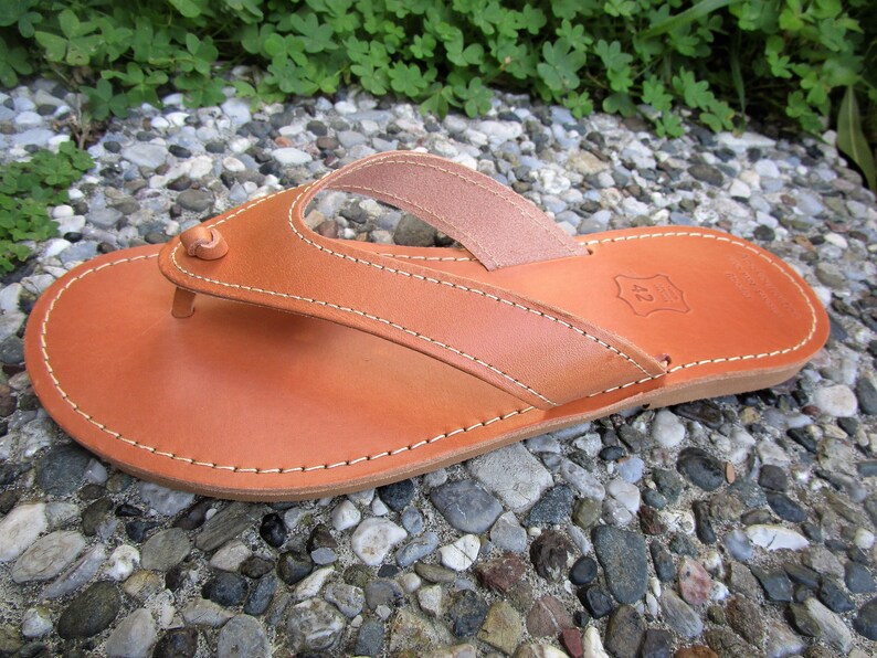 May include: A pair of brown leather thong sandals with a simple design. The sandals have a stitched edge and a leather strap that goes between the toes.