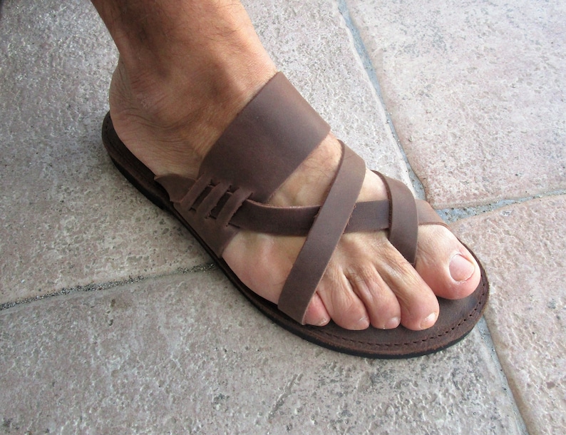 May include: Brown leather sandals with a criss-cross strap design. The sandals have a thong style toe strap and a flat sole.