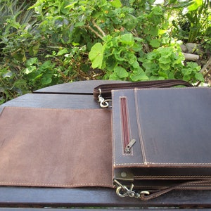 May include: A brown leather messenger bag with a flap closure and a zippered pocket on the front. The bag has a long adjustable strap and a metal clasp.