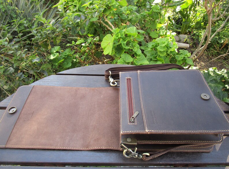 May include: A brown leather messenger bag with a flap closure and a zippered pocket on the front. The bag has a long adjustable strap and a metal clasp.