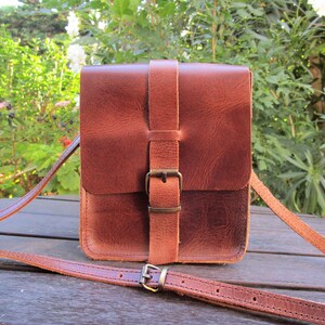 May include: A brown leather crossbody bag with a buckle closure and adjustable strap.