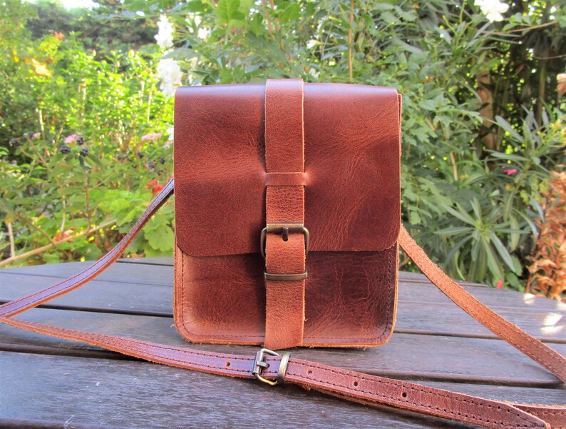 May include: A brown leather crossbody bag with a buckle closure and adjustable strap.