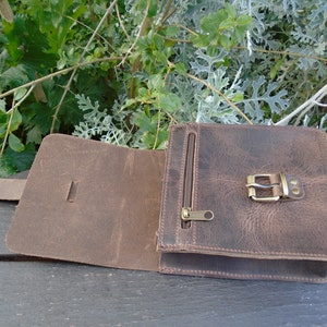 May include: A brown leather crossbody bag with a flap closure and a buckle. The bag has a zippered pocket on the front and a strap.