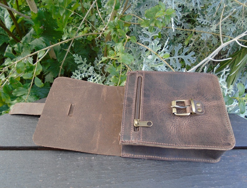 May include: A brown leather crossbody bag with a flap closure and a buckle. The bag has a zippered pocket on the front and a strap.
