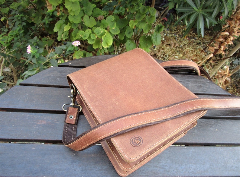 May include: A brown leather crossbody bag with a dark brown strap and a small brown logo on the front.